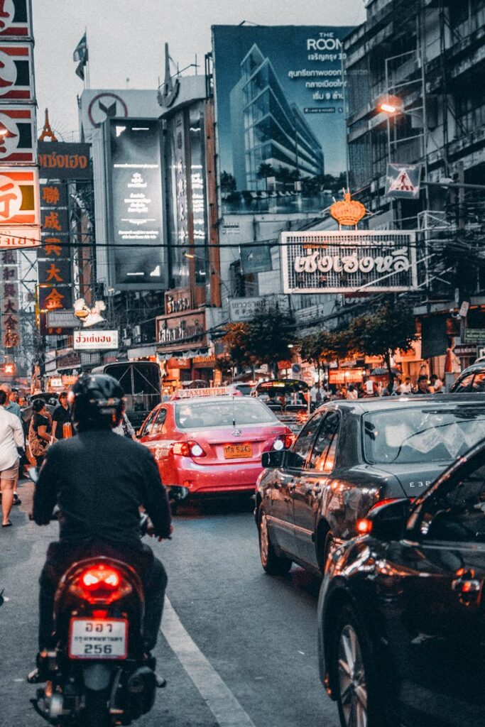 Dynamic scene of busy street life in Bangkok's Chinatown at night with cars and bustling crowds.